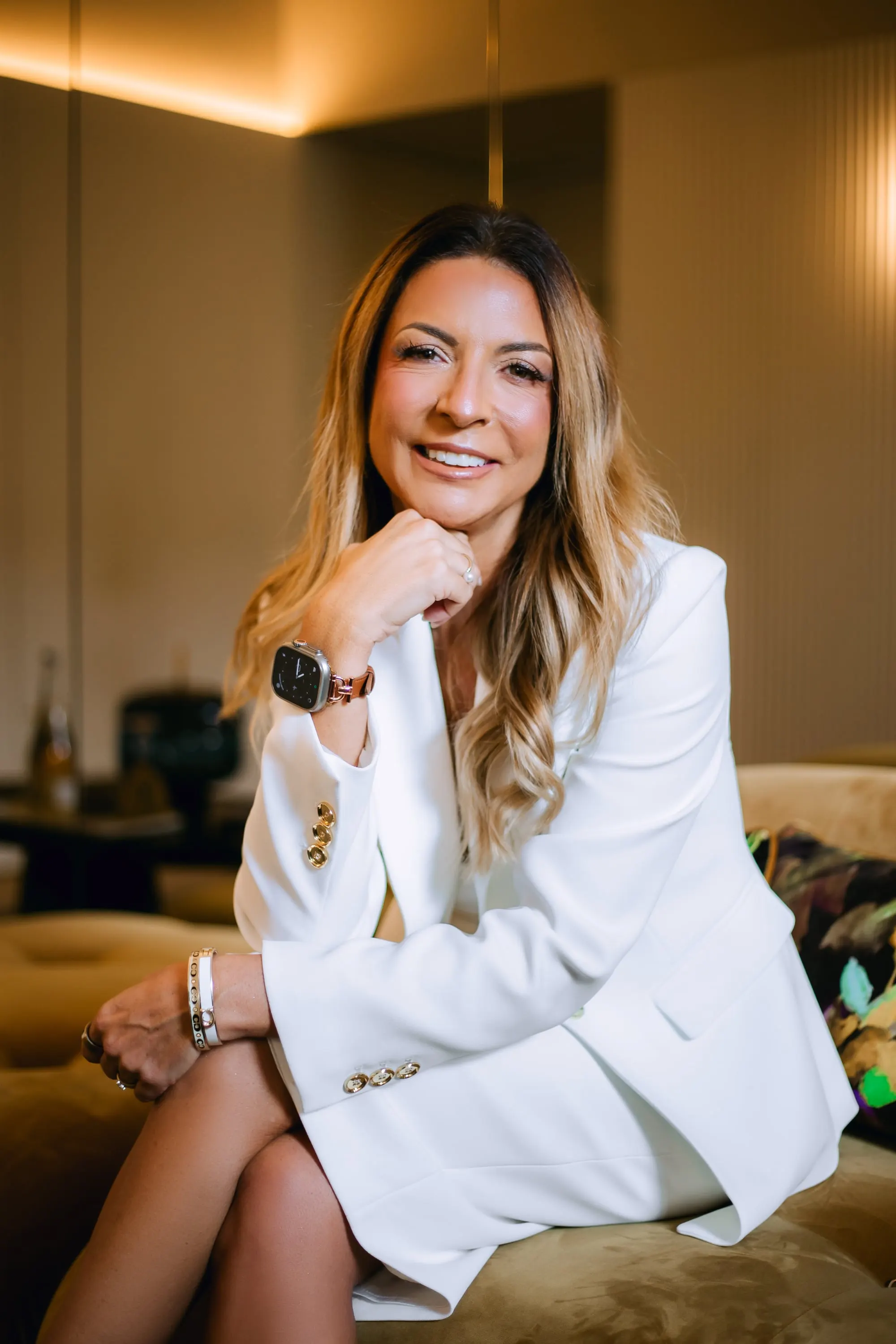 Sara Torres de casaco branco, sentada, a sorrir, com o queixo apoiado na mão.