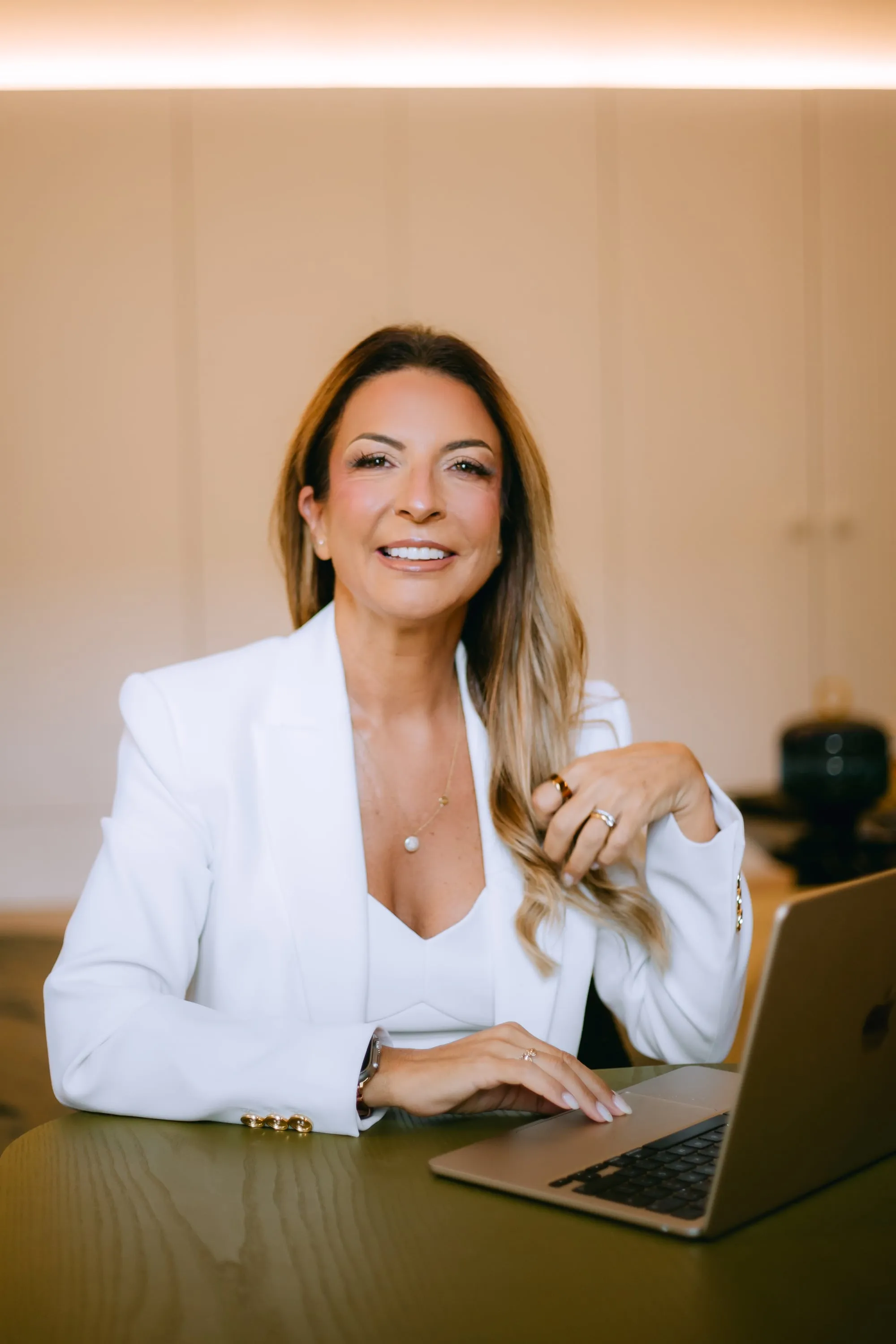 Sara Torres de casaco branco, a sorrir, sentada a uma mesa com o computador.