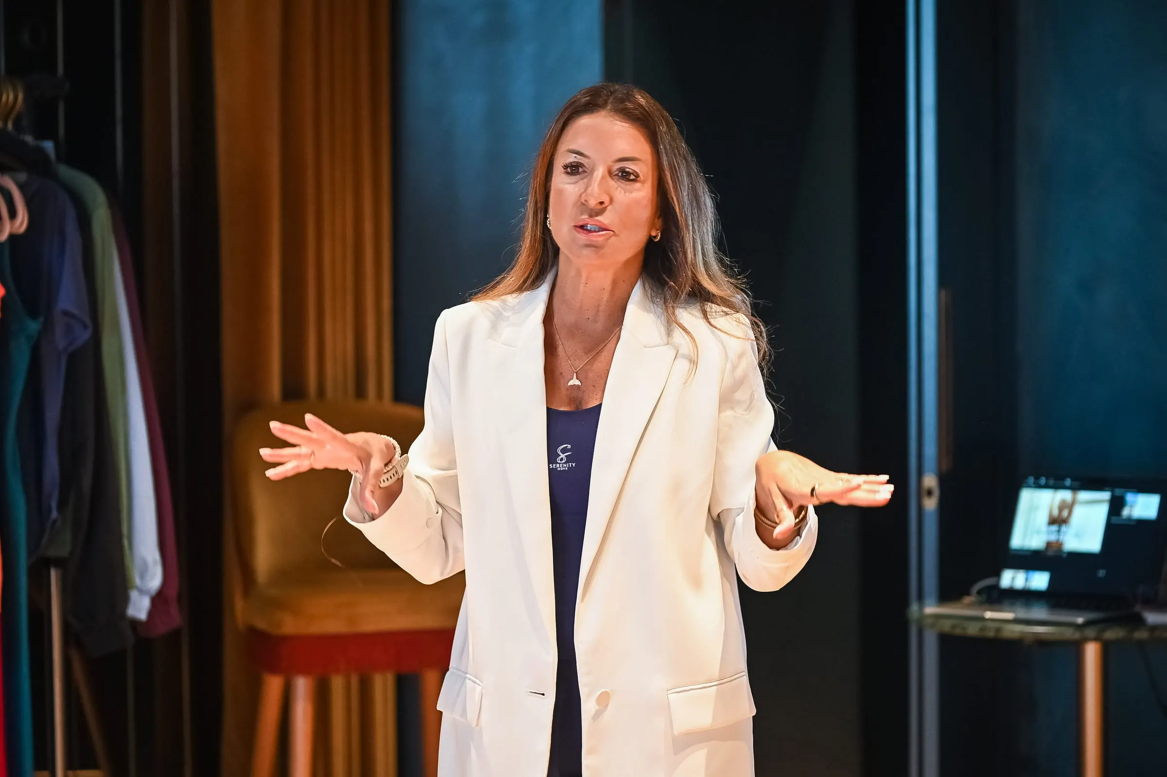 Sara Torres de casaco branco, a falar para uma sala, de braços abertos.