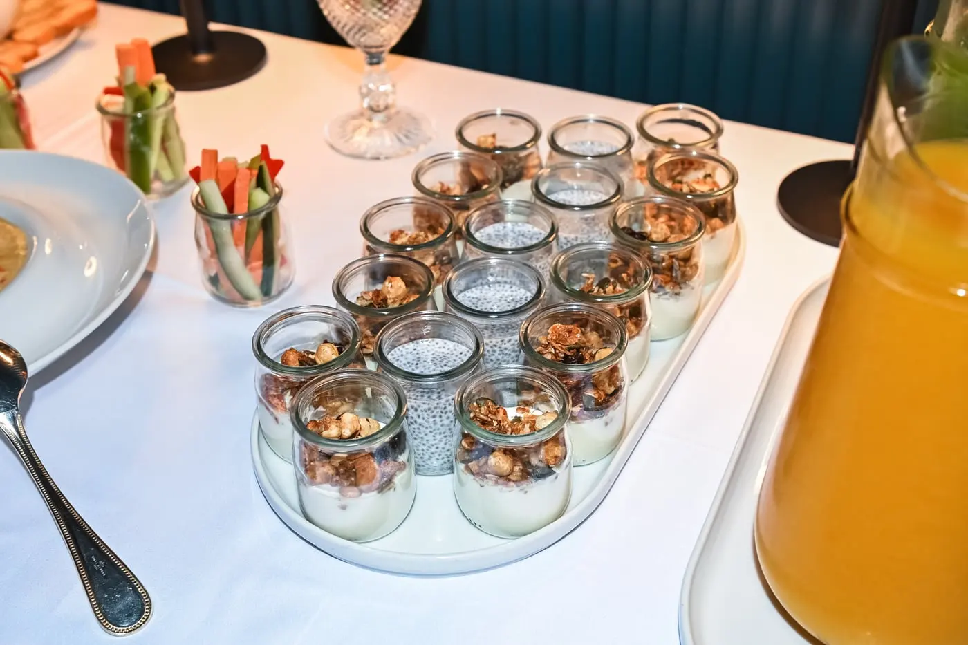 Frascos de iogurte com granola e um jarro de sumo, numa mesa de brunch.