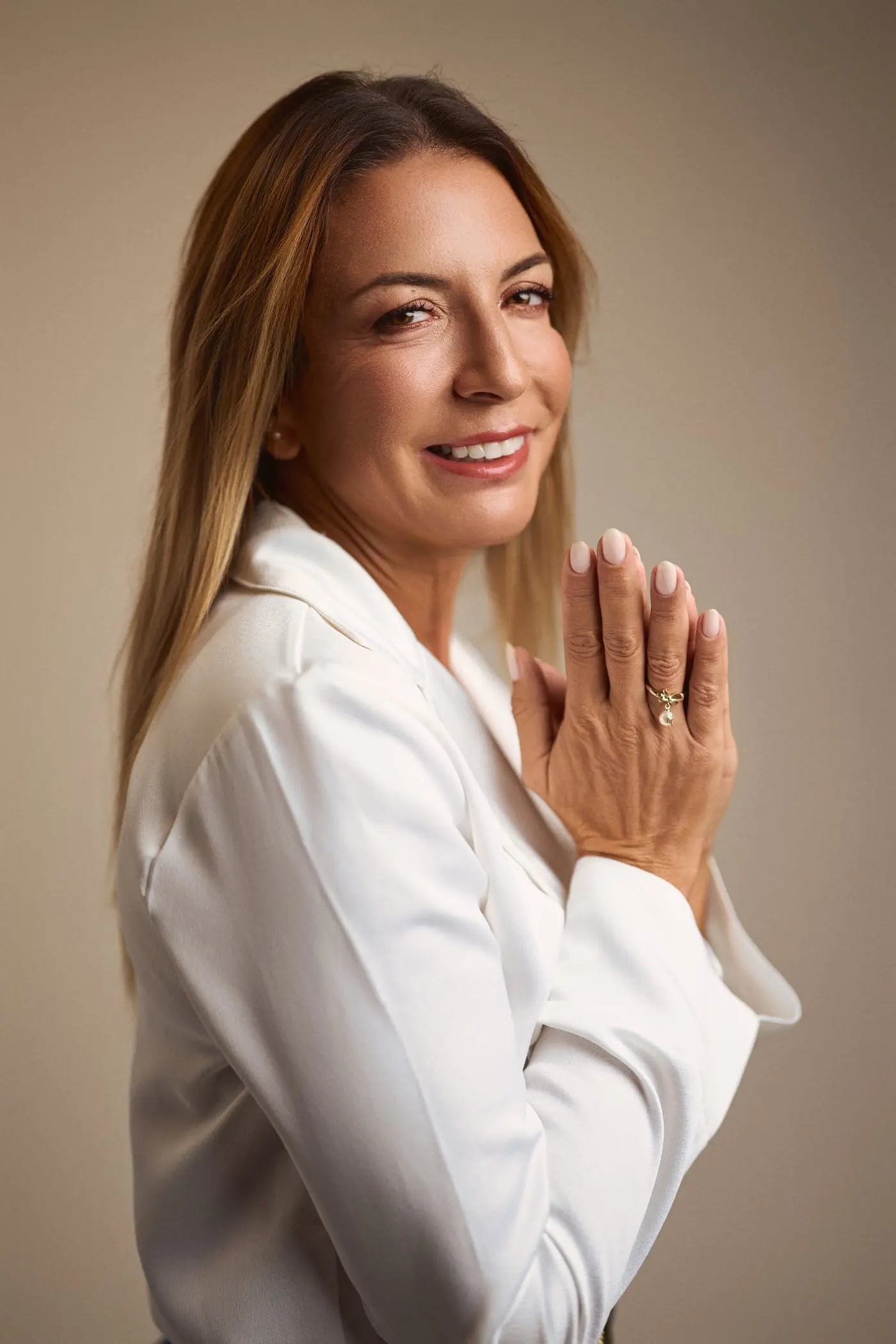 Sara Torres de perfil, a sorrir, com as mãos juntas à frente do rosto.