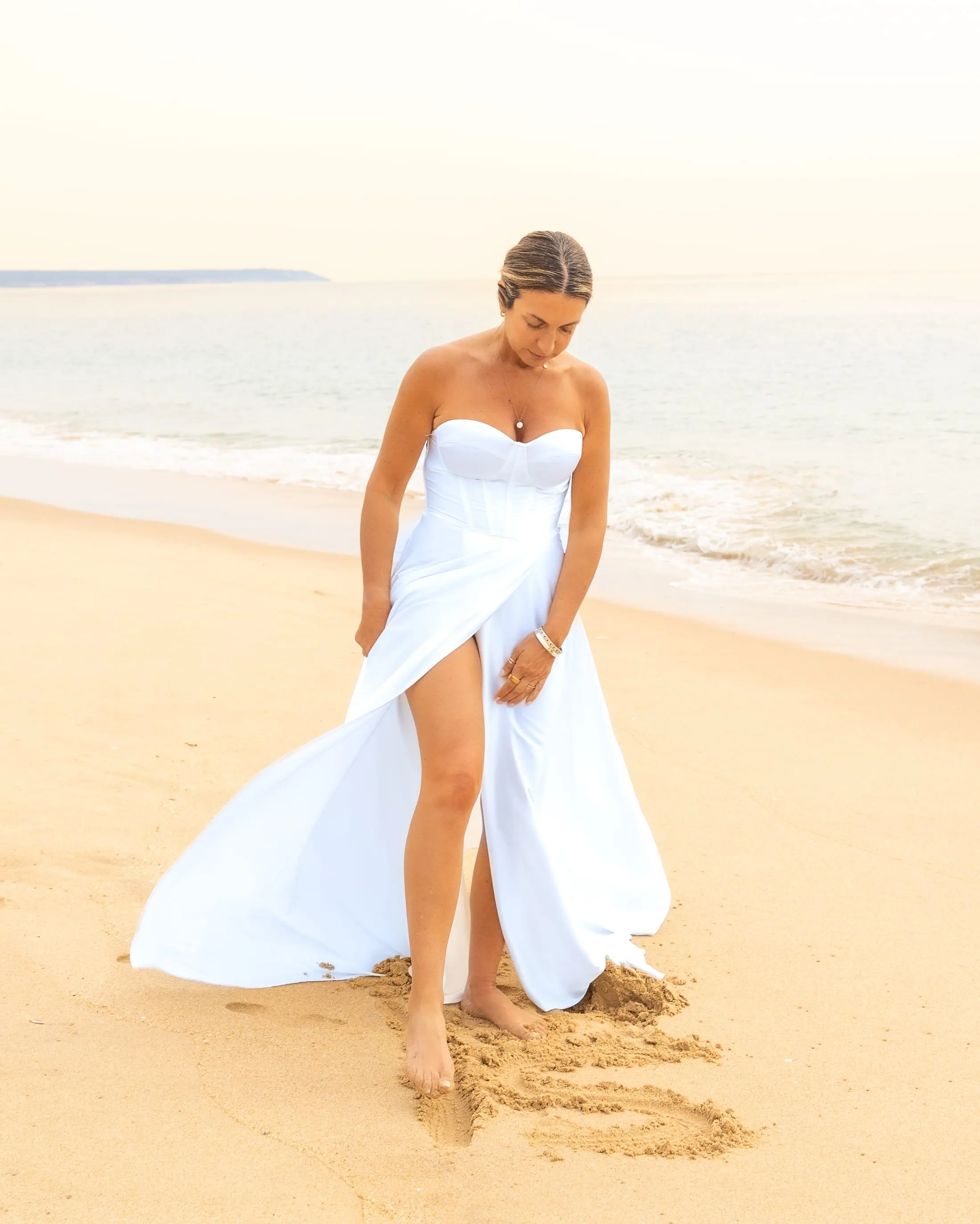 Sara Torres, de vestido branco, a desenhar na areia de uma praia.