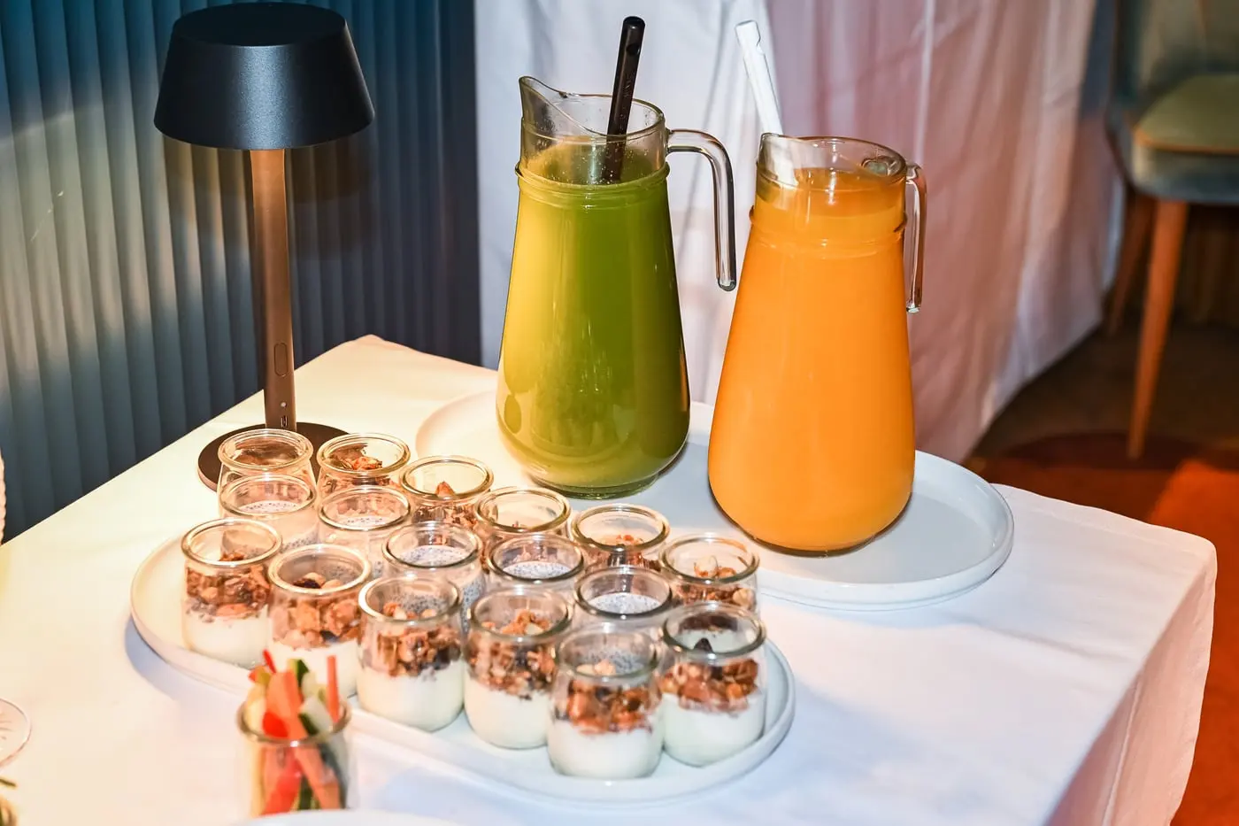 Jarros de sumo verde e de laranja e copos de iogurte com granola.