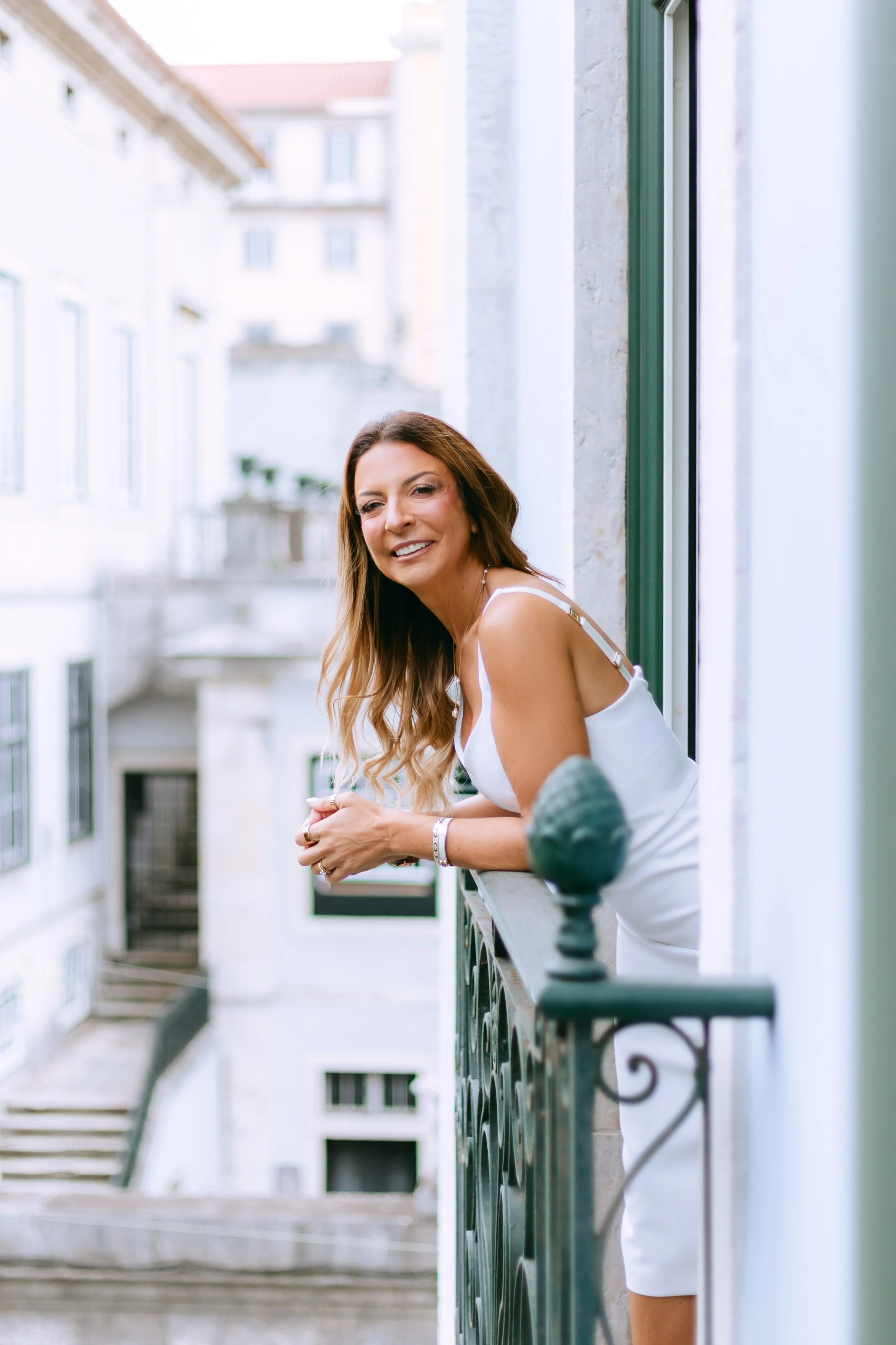 Sara Torres a sorrir, debruçada numa varanda, com uma rua de Lisboa ao fundo.
